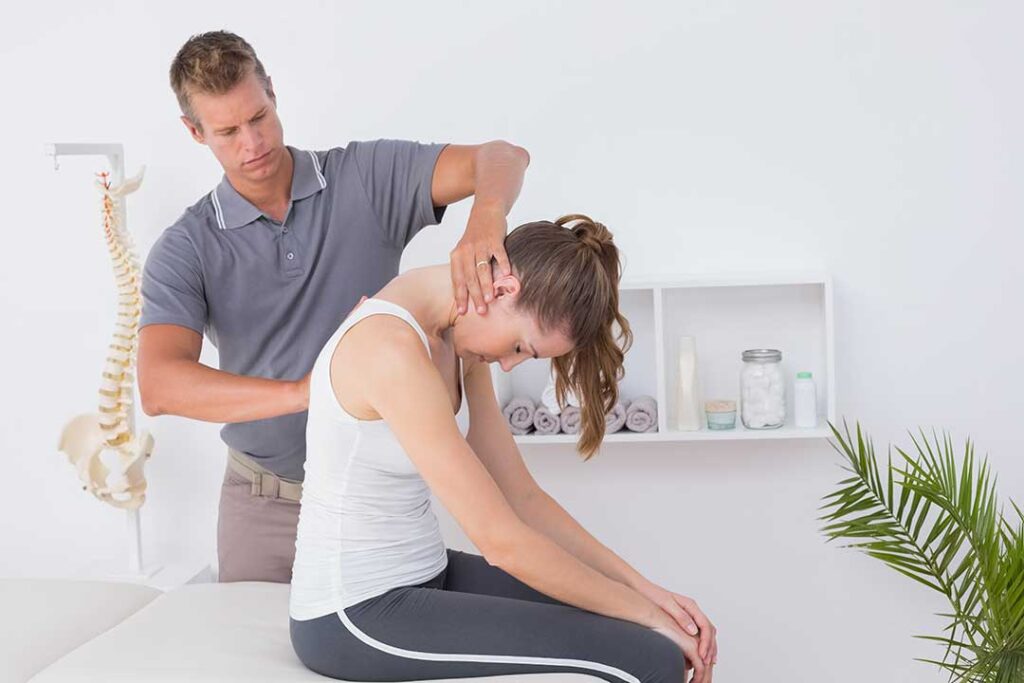A chiropractor gently examining a person's spine while they are seated in a comfortable clinical setting.
