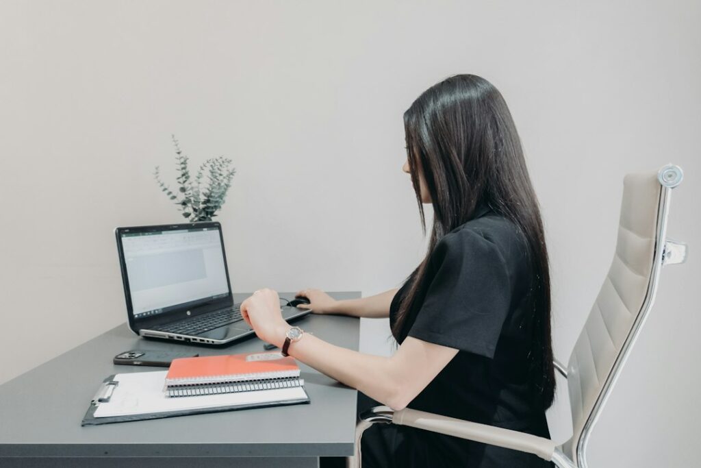 Child sits at a desk with supported feet, an eye-level laptop, notebook, and backpack nearby.